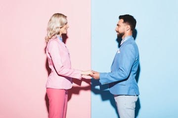 side view of smiling woman and handsome man holding hands on pink and blue background