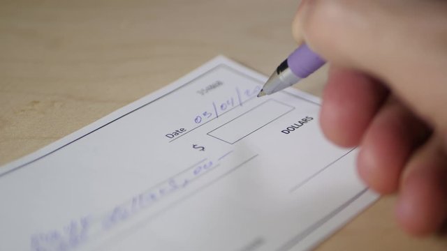 Close-up of a man's hand filling out a 1,000 dollars'Bank check.