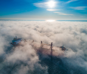 Naklejka na ściany i meble Cargo ship and cranes silhouettes in sea fog, crane vessel working for delivery of delivery containers.
