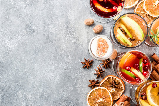 Various autumn or winter seasonal alcohol hot cocktails - mulled wine, glogg, grog, eggnog, warm ginger ale, hot buttered rum, punch, mulled apple cider on gray background, top view with copy space