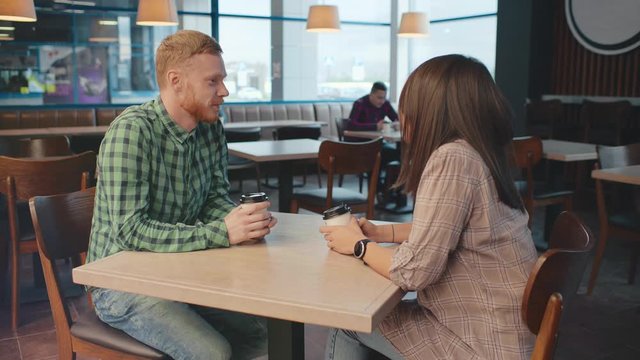 Love young couple sitting at restaurant cafe table with take away coffee cups. Caucasian redhead man with his girlfriend or colleague at lunch break. First date in restaurant