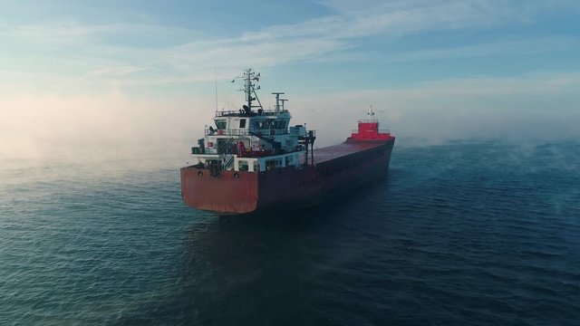 Cargo ship sailing on open sea water and beautiful sunrise, aerial drone view