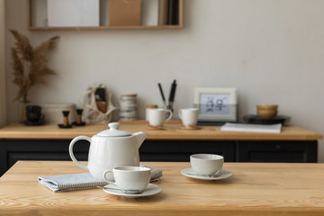 Fototapeta na wymiar Cute white teapot and white cups on table ready for tea drinking in light kitchen