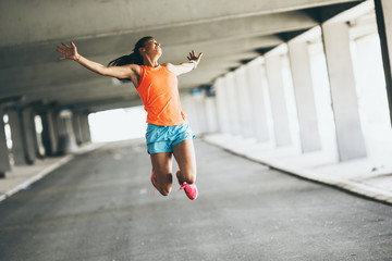 Young female runner jumps on the street,expressing positive emotion.She made her goal of the day.Fitness and workout concept.	