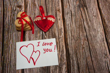 The Concept Of Valentine's Day. Homemade cakes for the holiday. A heart-shaped cookie tied with a ribbon, a hand-sewn textile heart and a note with a Declaration of love on a wooden background.