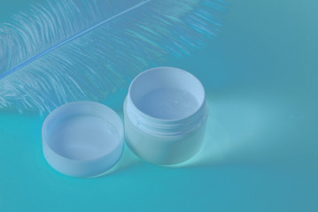 Big white feather and white and cream jar closeup macro neon blue inverted colored. Skin care concept