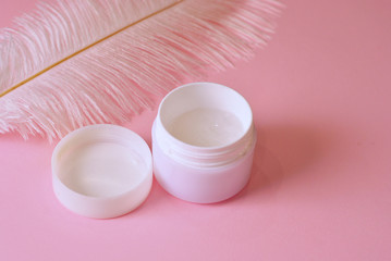 Big white feather and white and cream jar closeup macro. Skin care concept
