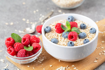 Healthy breakfast - oatmeal with fresh berries in a bowl. Oatmeal porridge with blueberries, raspberries and mint.
