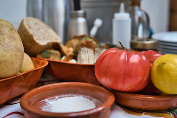 Still life of organic and fresh natural vegetables. Potatoes, tomatoes, lemon, bread, harina, mushrooms, vegetables and some kitchen pots in the background out of focus