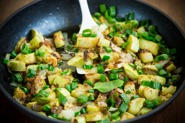 zucchini fried with onions and herbs in a pan on a wooden table