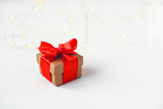 Gift box with a red bow on a background of blurred lights garland.