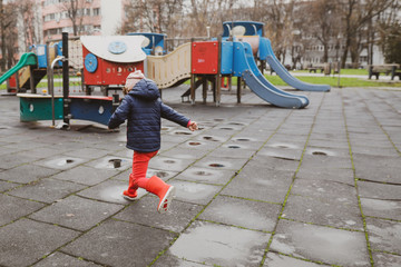 Little girl playing and jumping in rain puddle on an empty kids playground during a winter day in Bucharest, Romania.