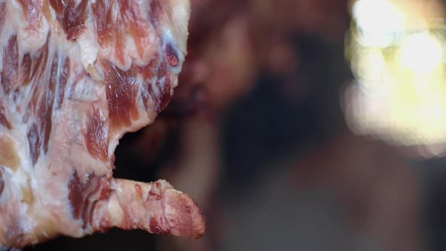 Ham and bacon hanging and drying in smokehouse on traditional way on blue smoke.  The sunrays pierce through the blue smoke.