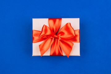 Cardboard gift box with red bow on blue background.
