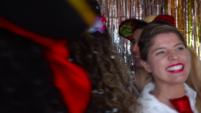 Group of dressed friends are dancing at carnival party. Camera walks back revealing the revelers. Men and women having fun.