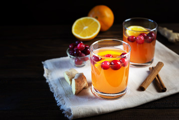 Two glasses orange and cranberry non-alcoholic punch with orange slices and spice on a dark wooden table.
