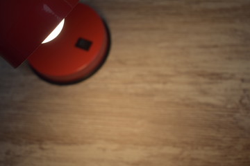 
White bulb in red lamp, illuminating part of a desk table