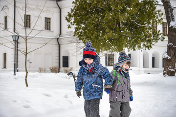 Two little kid boys in colorful clothes, outdoors during snowfall. Active outdoors leisure with children in winter on cold snowy days. Happy siblings having fun with snow. Travel in winter city