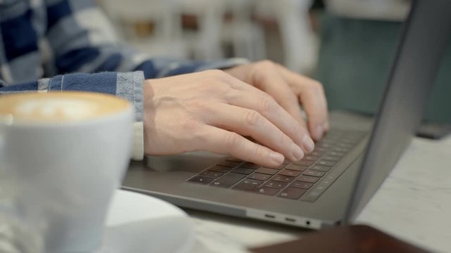 Male hands type on laptop keyboard in cafe