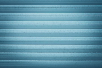 Blue metallic jalousie. Texture of corrugated metal surface. Dirty ribbed background with straight lines. Striped wall, space. Exterior element.