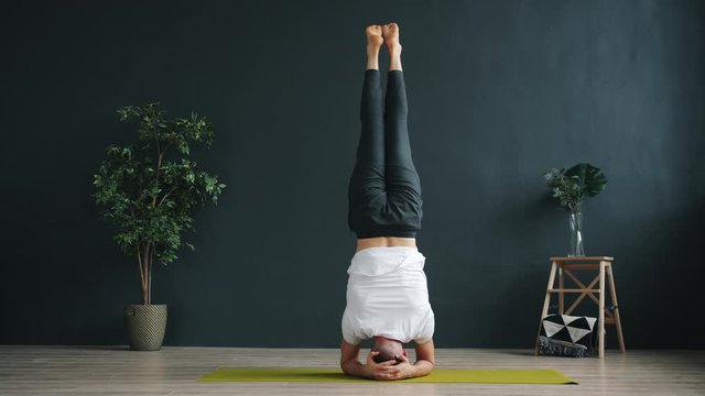 Slow motion of advanced yoga student in sportswear doing headstand working out in studio alone focused on exercise. Bodycare, sports and occupation concept.