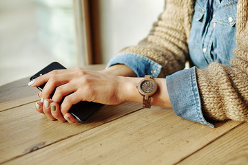A woman sits at a table with phones in her hands. A wrist watch is worn on the wrist. The face is not visible.