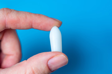 White suppository for anal or vaginal use in patient's hand on blue background. Medical candles for...