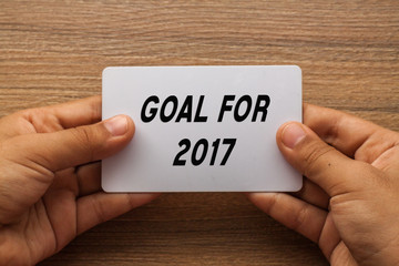 Goal For 2017 written on card with hand holding it with wood background