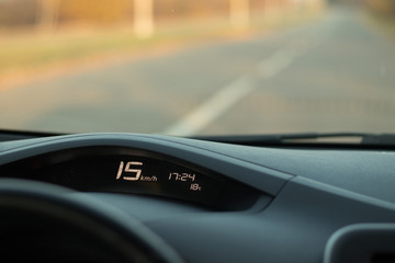 Obraz na płótnie Canvas The dashboard of the car with a speed of 15 km / h on the speedometer, time, temperature and blured road on background; safe driving concept; speed limit; copy space; anomaly warm