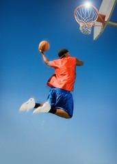 Man Dunking Basketball Into Hoop Against Blue Sky