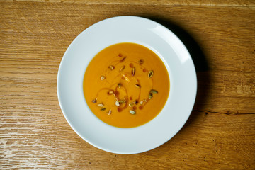 Tasty and homemade pumpkin cream soup in a white plate on a wooden background. Healthy lunch for proper diet. Top view, flat lay food