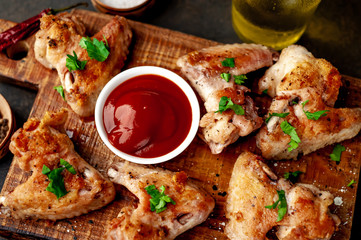 grilled chicken wings on a cutting board with spices and herbs on a stone background
