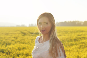 Fototapeta na wymiar Portrait of young woman with long hair in strong afternoon backlight sun, blurred field with yellow flowers background