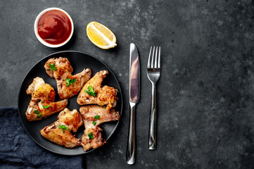 grilled chicken wings on a black plate with spices and herbs on a stone background with copy space for your text