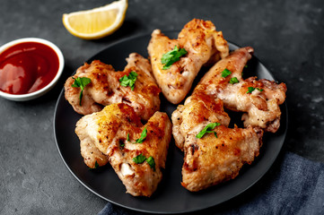 grilled chicken wings on a black plate with spices and herbs on a stone background with copy space for your text