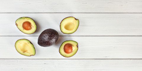 Fototapeta na wymiar Ripe brown avocado - Hass bilse variety - halved and arranged on white boards desk, view from above, space for text right side