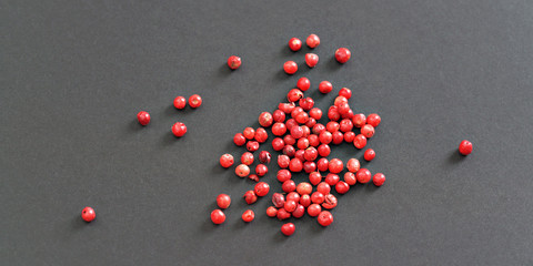 Whole pink / red peppercorns on black / gray paper, view from above