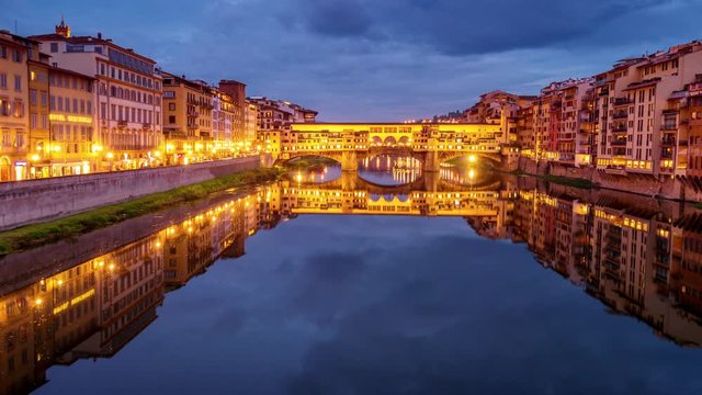Ponte Vecchio bridge in Florence, Italy is illuminated as night falls, time lapse, logos blurred for commercial use
