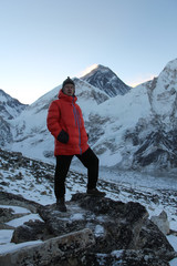 Caucasian man in traditional nepalese hat and red down jacket stands on the slope of Kala Patthar mountain just before sunrise. Blurred Mount Everest in the background. Travel in Nepal theme
