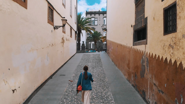 Aerial view - young stylish girl walking along a narrow street of the old Spanish city, top view.