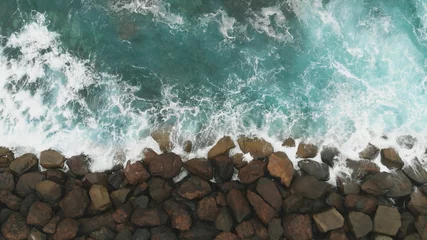  Bovenaanzicht. De constructie van stenen om de kust te versterken en te beschermen tegen de oceaan - in vogelvlucht. Grote stenen en de oceaan van turquoise kleur. © Artem