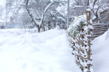 Winter old shabby wobbly wicker fence made of wooden boards. Snow blizzard