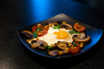Freshly fried scrambled eggs with vegetables on a black plate