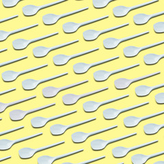 white plastic tea spoons pattern on yellow background