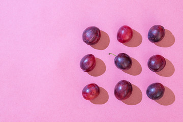 The pattern of blue homemade plums lie the same on a pink background and one yellow plum.  Flat lay, top view, copy space