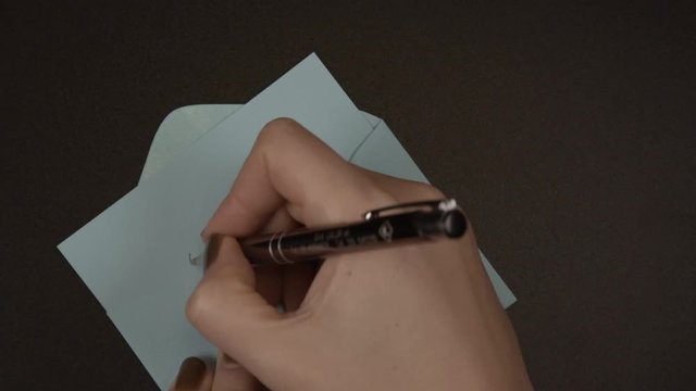 Female hand writes a pen "goodbye" on paper and puts it in a blue envelope. The concept of parting and parting with the past, close up