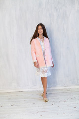 Portrait of a beautiful fashionable girl in a pink jacket and white dress