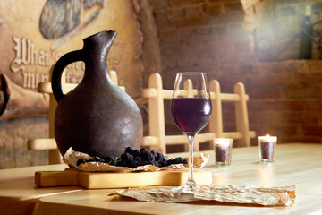 Glass of red wine, mulberry, clay jug on wooden table in a wine cellar restaurant