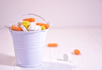A bucket of multi-colored pills on a white wooden background with space for text.