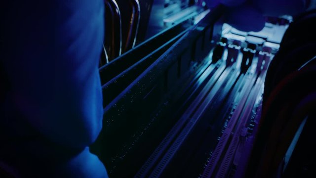 Close-up Moving Macro Shot: Person's Hands Installs RAM Memory into Computer Motherboard Slot. Technician Upgrades PC / Server Hardware. Modern High-End PC Shot in Stylish Neon, Pink-Blue Colors. 